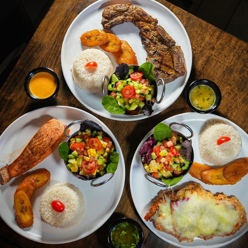 Three Ecuadorian dishes with grilled meat, salmon, and fried chicken, each served with rice, plantains, and salad.