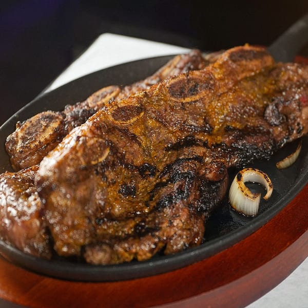 Grilled short ribs with charred onions served on a sizzling cast iron platter at Sabor Latino.