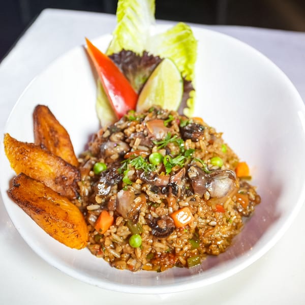 Ecuadorian mushroom rice with peas, carrots, and plantains, garnished with lettuce, lime, and red pepper.