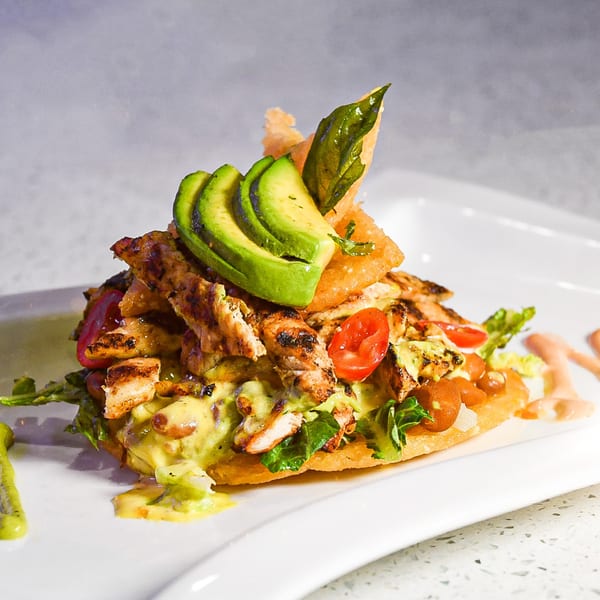 Grilled chicken, avocado, and cherry tomatoes on a crispy tortilla with green and pink sauces.