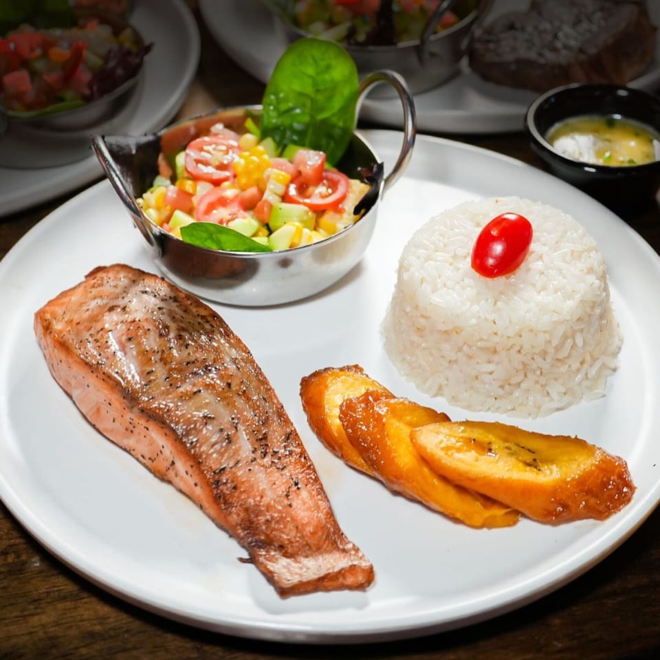 Sabor Latino's grilled salmon with rice, fried plantains, and a side of fresh corn and tomato salad.