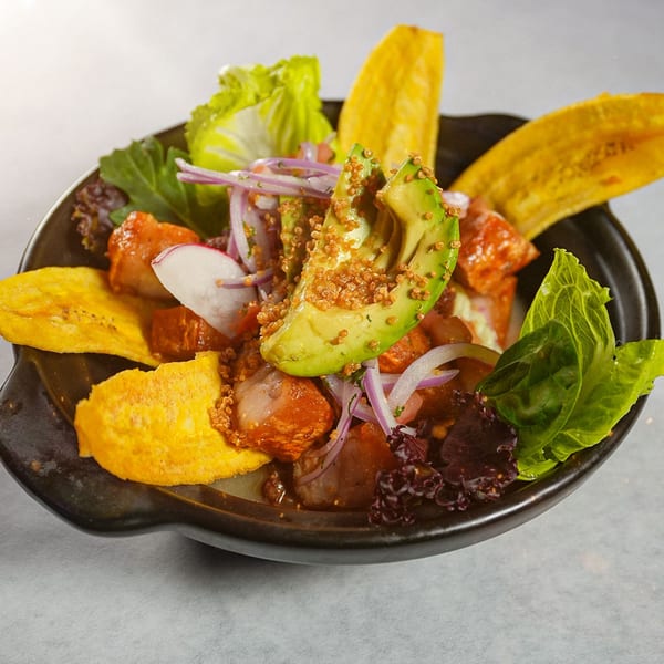 Ecuadorian ceviche with avocado, red onion, lettuce, and plantain chips in a dark bowl.