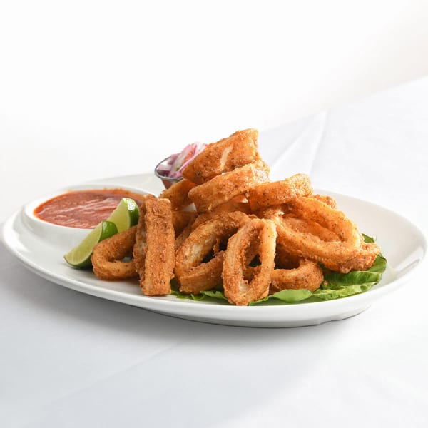 Crispy fried calamari rings on lettuce with lime wedges, red sauce, and pickled onions.