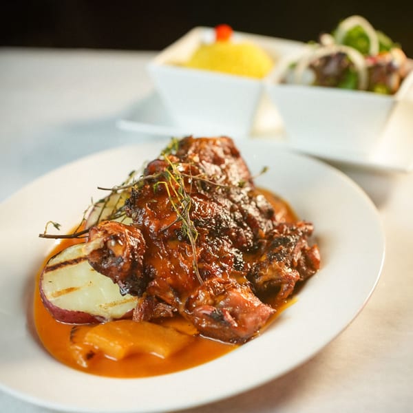 Ecuadorian grilled chicken with sauce, grilled potatoes, and two side dishes in white bowls.