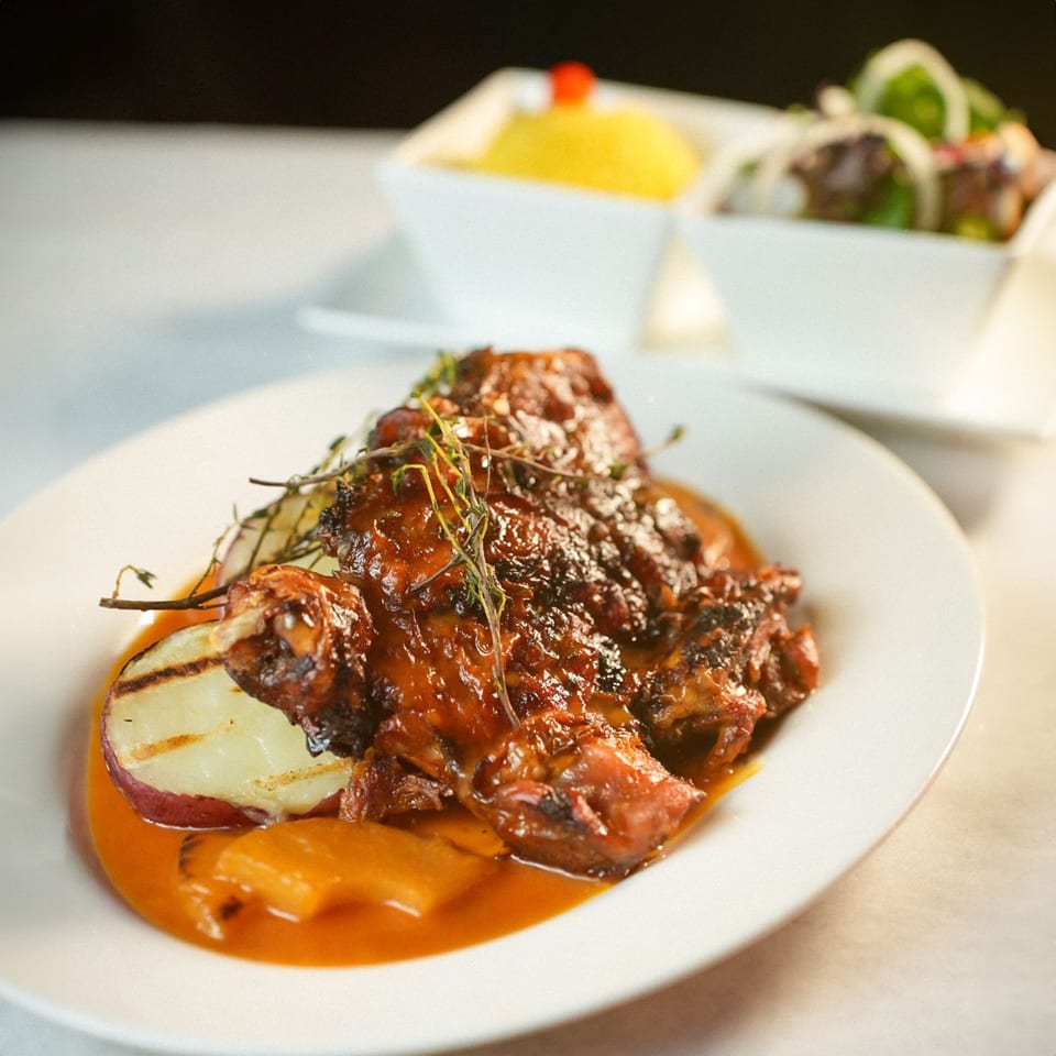 Ecuadorian grilled chicken with sauce, grilled potatoes, and two side dishes in white bowls.