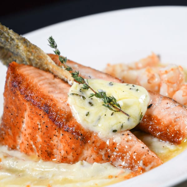 Grilled salmon with a dollop of herb butter, crispy skin, and shrimp in a creamy sauce.