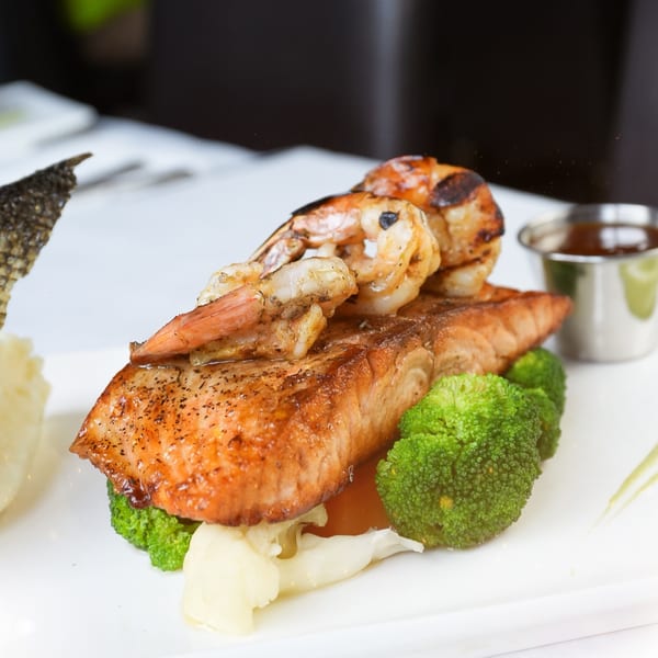Grilled salmon and shrimp with broccoli and mashed potatoes, served with a side of sauce.
