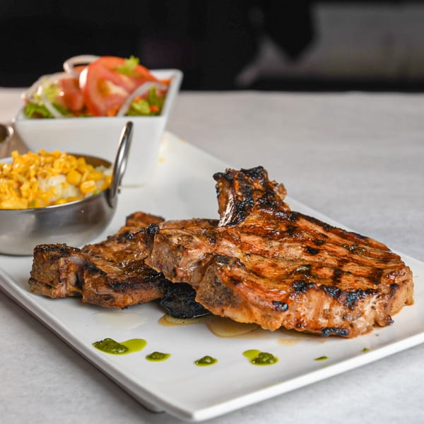 Grilled pork chops with corn, mashed potatoes, and a side salad on a white plate.