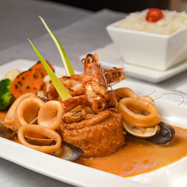 Ecuadorian seafood dish with shrimp, calamari, mussels, and vegetables in a rich orange sauce.
